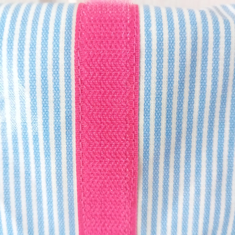 May include: Close-up of a pink fabric strip sewn onto a blue and white striped fabric. The fabric has a textured appearance.