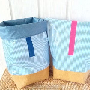 May include: Two blue and white striped fabric storage bins with a brown bottom. One bin has a blue trim and the other has a pink trim.
