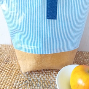 May include: A blue and white striped fabric lunch bag with a brown leather bottom. The bag has a blue fabric handle.