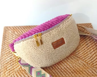 May include: A crescent-shaped fanny pack featuring a top panel of magenta corduroy and a main body of beige sherpa fleece. It includes gold-tone metal zippers and a brown leather-like patch with the text frech wild wunderbar.