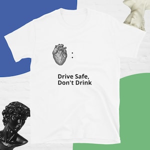 Puede incluir: Camiseta blanca con una ilustración en blanco y negro de un corazón y el texto "Conduce con seguridad, no bebas."