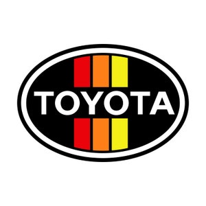 May include: A black and white oval logo with the word "TOYOTA" in white letters. There are three vertical stripes in the center of the logo, red, orange, and yellow.