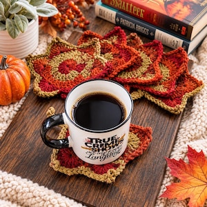 May include: A white ceramic mug with a black handle and the text "TRUE CRIME SHOWS are my love language" sits on a star-shaped crochet coaster. The coaster features a gradient of red, orange, and gold yarn. Additional matching coasters are stacked nearby.