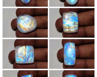 May include: Eight polished moonstone gemstones in various shapes, including oval, teardrop, and rectangular. The stones display a shimmering, iridescent play of color, with hues of blue, white, and yellow. The gemstones are displayed against a neutral background.