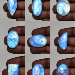 May include: Nine polished moonstone gemstones in various shapes, including oval, teardrop, and rectangular. The stones display a shimmering, iridescent blue and white color with internal patterns. The gemstones are held in a hand.
