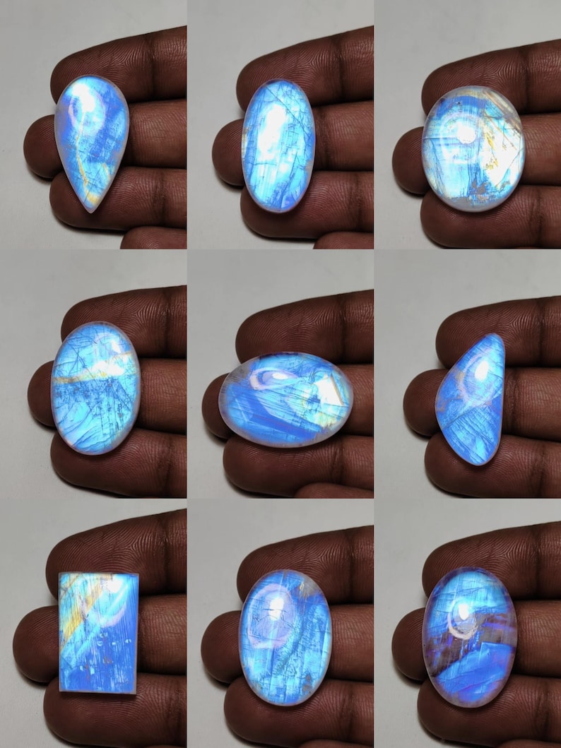 May include: Nine polished moonstone gemstones in various shapes, including oval, teardrop, and rectangular. The stones display a shimmering, iridescent blue and white color with internal patterns. The gemstones are held in a hand.