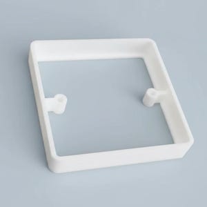 Op de afbeelding: Een wit, vierkant kunststof frame met afgeronde hoeken. Twee kleine cilindrische uitsteeksels bevinden zich aan weerszijden van het frame. Het object staat tegen een lichtblauwe achtergrond.