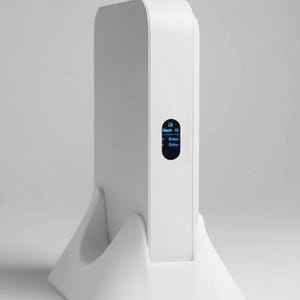 May include: A white electronic device with a small screen displaying data, set in a matching white stand. The device has a sleek, modern design, and the screen shows the text "Only Breathe Me".