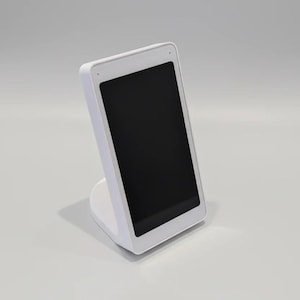 Op de afbeelding: Een wit digitaal weergaveapparaat met een zwart scherm, gemonteerd op een witte standaard. Het apparaat heeft afgeronde hoeken en een kleine camera of sensor aan de bovenkant. De standaard heeft een solide, gebogen vorm.