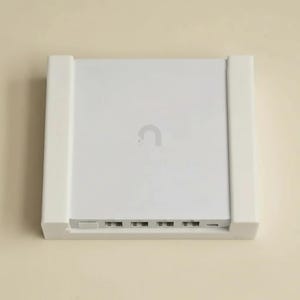 May include: A white electronic device with a curved logo on the top. The device has several ports along the bottom edge and is encased in a white frame. The background is a light beige colour.