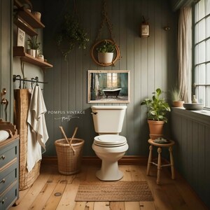 Peut inclure: Des toilettes blanches avec un couvercle ferm&eacute; dans une salle de bain aux murs verts et au sol en bois. Une estampe encadr&eacute;e d'une salle de bain vintage avec une baignoire est accroch&eacute;e au mur. Une plante en pot est pos&eacute;e sur un petit tabouret en bois.