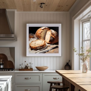 May include: A framed painting of a still life featuring a loaf of freshly baked bread sliced open, revealing the soft, golden interior. The bread is arranged on a white cloth with a knife nearby, creating a simple yet elegant composition.