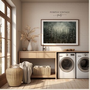 May include: A white laundry room with a wooden countertop and two white washing machines. A framed print of a snowy forest hangs on the wall above the countertop. The print is titled "POMPUS VINTAGE prints".
