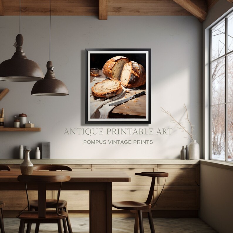 May include: A framed print of a still life featuring a loaf of freshly baked bread sliced open, resting on a white cloth with a wooden cutting board and a knife. The print is set against a rustic kitchen backdrop with a wooden table and chairs.