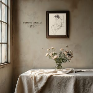 May include: A framed black and white drawing of a woman sitting in a chair. The drawing is on a light beige wall above a white table with a white tablecloth. A vase with white flowers sits on the table.