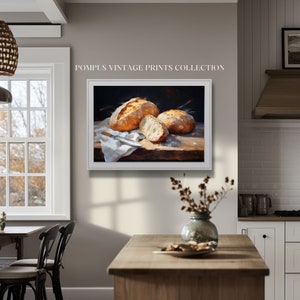 May include: A painting of three loaves of bread on a wooden table. The bread is golden brown and crusty. The painting is in a white frame.