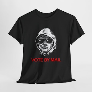 Op de afbeelding: Zwart t-shirt met een grijswaarden illustratie van een persoon met een zonnebril en een hoodie. De rode tekst "VOTE BY MAIL" is eronder gedrukt. Het t-shirt is gemaakt van een zachte stof.