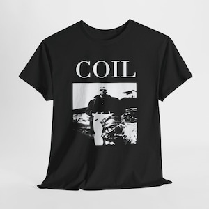 Puede incluir: Una camiseta negra de manga corta con la palabra COIL en letras mayúsculas blancas sobre un estampado gráfico en blanco y negro. El gráfico muestra a una persona de pie con abrigo oscuro y pantalones claros junto a un elemento texturizado.
