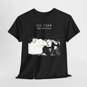Puede incluir: Una camiseta negra de manga corta con un estampado gráfico blanco de una persona tumbada. El texto DIE FORM y l'âme électrique está impreso en blanco sobre el gráfico. El diseño tiene una estética en blanco y negro de alto contraste.