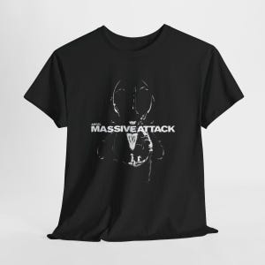 May include: Black t-shirt featuring a white graphic design and the text "ANGEL MASSIVE ATTACK". The design is a stylized, abstract image. The shirt has short sleeves and a crew neck.