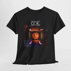 Puede incluir: Una camiseta negra de manga corta con un estampado gráfico en el pecho. El diseño incluye la palabra COIL en texto blanco sobre una imagen cuadrada central de un orbe naranja brillante rodeado por cuatro pequeñas manos humanas.