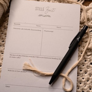 Puede incluir: Una hoja de papel blanca con las palabras "STILLE Zeit" en la parte superior. El papel está dividido en secciones con encabezados para "Bibelstelle", "Thema", "Historischer oder kultureller Zusammenhang", "Hauptaussage", "Datum", "Wie kann ich diese Wahrheit anwenden? Gibt es eine bestimmte Handlung oder Entscheidung, die ich ändern sollte?", "Wofür bin ich Gott dankbar?" y "Gebet". Un bolígrafo negro con la palabra "Jesus" en él está sobre el papel.