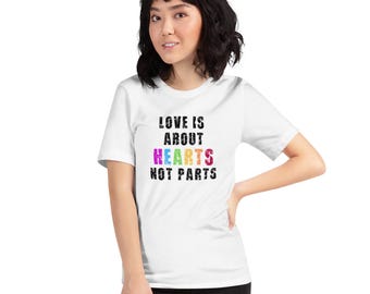 May include: White t-shirt with the text "LOVE IS ABOUT HEARTS NOT PARTS" in black and colorful letters. The shirt is short-sleeved and has a crew neck.