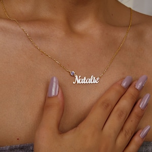 Peut inclure: Collier en chaîne dorée avec un pendentif en métal blanc portant le nom "Natalie" et une petite pierre précieuse violette.