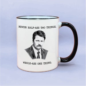 May include: White ceramic coffee mug with a black handle and black rim. The mug features a black and white illustration of a man with a mustache and the text "NEVER HALF-ASS TWO THINGS. WHOLE-ASS ONE THING."