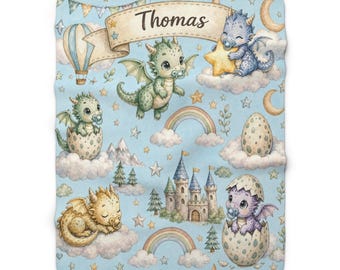 May include: A light blue baby blanket featuring a repeating pattern of colorful dragons, castles, rainbows, and stars. A central banner displays the name Thomas. The dragons are depicted with pacifiers, some emerging from eggs or sitting on clouds.