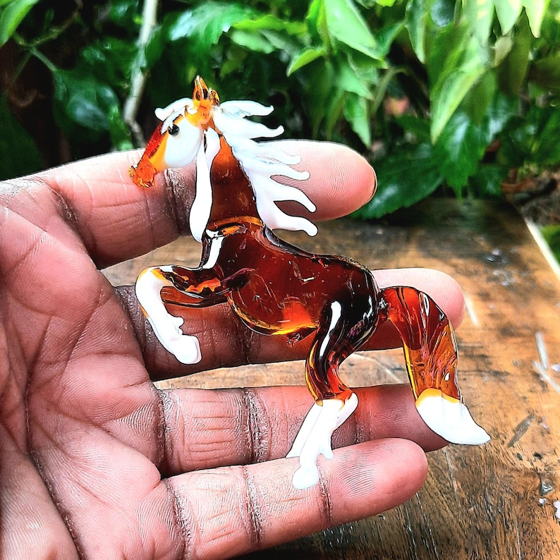 May include: A brown glass horse figurine with white mane and tail. The horse is standing on its hind legs with its front legs raised.