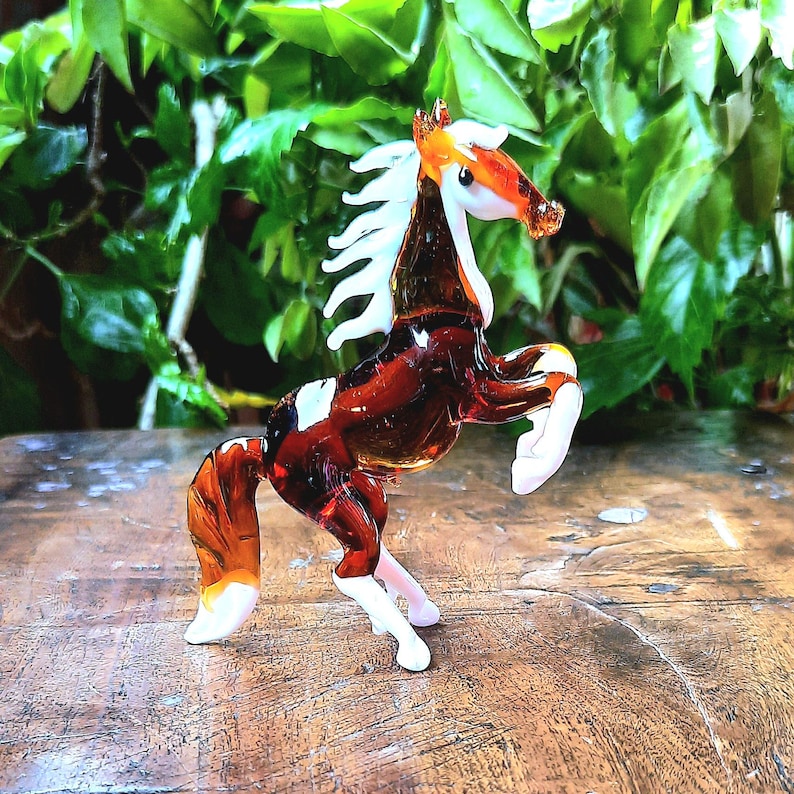 May include: A brown and white glass horse figurine with a white mane and tail. The horse is standing on its hind legs with its front legs raised.