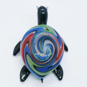 May include: A colourful glass turtle figurine with a swirling pattern of red, blue, green and black on its shell. The turtle has a black body and head.