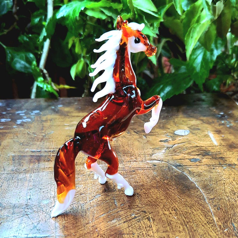May include: A brown glass horse figurine with white mane and hooves. The horse is standing on its hind legs with its front legs raised.
