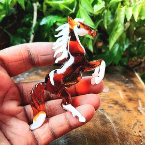May include: A brown and white glass horse figurine with a white mane and tail. The horse is standing on its hind legs with its front legs raised.