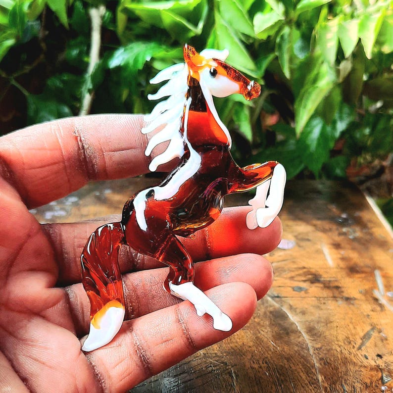May include: A brown and white glass horse figurine with a white mane and tail. The horse is standing on its hind legs with its front legs raised.