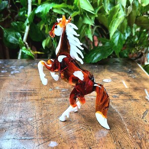 May include: A brown and white glass horse figurine with a white mane and tail. The horse is standing on its hind legs with its front legs raised in the air.