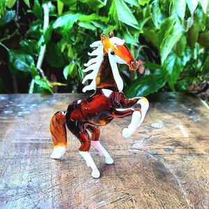 May include: A brown and white glass horse figurine with a white mane and tail. The horse is standing on its hind legs with its front legs raised in the air.