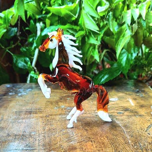 May include: A brown glass horse figurine with white accents. The horse is standing on its hind legs with its front legs raised. The figurine is made of glass and has a glossy finish.