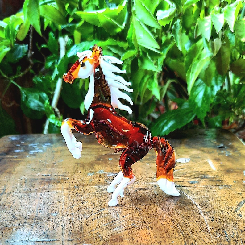 May include: A brown glass horse figurine with white accents. The horse is standing on its hind legs with its front legs raised. The figurine is made of glass and has a glossy finish.
