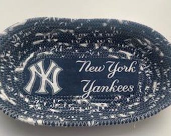 May include: A blue and white oval-shaped woven basket with a fabric patch featuring the New York Yankees logo and the text "New York Yankees".