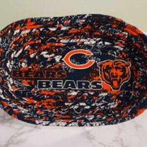 May include: Oval-shaped fabric basket with a navy blue, orange, and white pattern. The basket features the text "BEARS" and a logo of a bear's head and the letter "C" in orange.