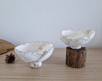 May include: Two white ceramic bowls with a textured surface. The bowls are shaped like mushrooms and have a raised base. One bowl is sitting on a wooden stump.