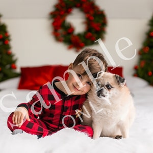 May include: A young boy in red and black plaid pajamas sits on a white bed with a small dog. The boy is smiling and has his arm around the dog. There are two Christmas trees in the background.
