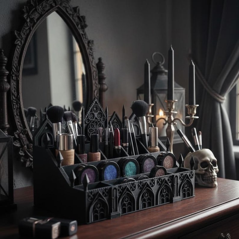 May include: A black gothic-style makeup organizer filled with brushes, eyeshadows, and lipsticks. The organizer sits on a wooden surface, next to a skull and a decorative mirror. Candles and a lantern are in the background.