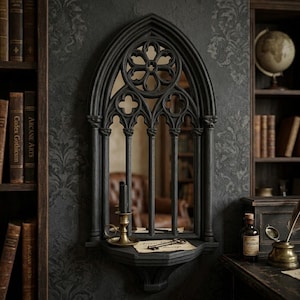 Könnte beinhalten: Ein schwarzer Spiegel im gotischen Stil mit einem gewölbten oberen Teil und aufwendigen Verzierungen. Der Spiegel hat eine Ablage mit einer Kerze, einem Schlüssel und einem Papier mit Text. Er ist an einer dunklen Wand befestigt, mit Bücherregalen und einem Schreibtisch im Hintergrund.