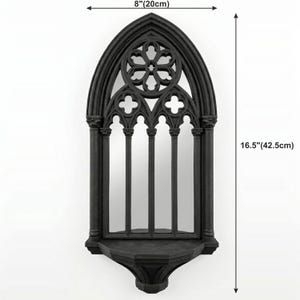 May include: Black gothic-style wall mirror, 16.5 inches (42.5cm) tall and 8 inches (20cm) wide. The mirror features an arched top with a decorative floral design and a shelf at the bottom. The frame has a detailed, textured finish.