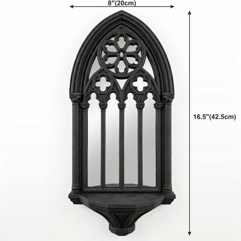 May include: Black gothic-style wall mirror, 16.5 inches (42.5cm) tall and 8 inches (20cm) wide. The mirror features an arched top with a decorative floral design and a shelf at the bottom. The frame has a detailed, textured finish.