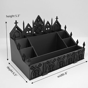 May include: Black desk organizer with a gothic cathedral design. The organizer is 8 inches wide, 6.3 inches deep, and 5.3 inches high. It features multiple compartments and decorative architectural details, including arched windows and crosses.