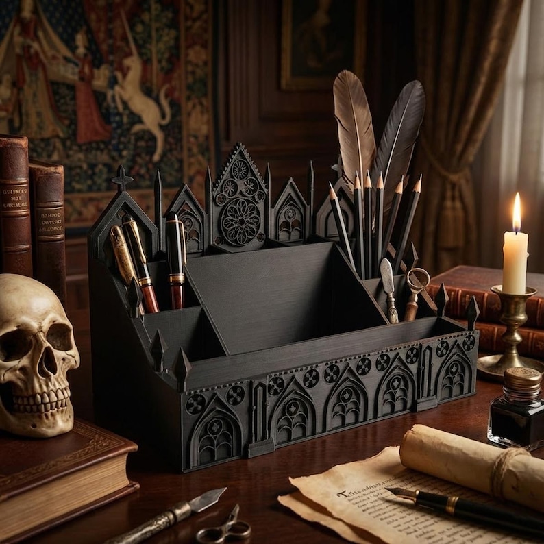 May include: A black gothic-style desk organizer with multiple compartments for pens, pencils, and other stationery items. The organizer features intricate architectural details, including arched windows and decorative elements. A skull, books, and a lit candle are also visible.